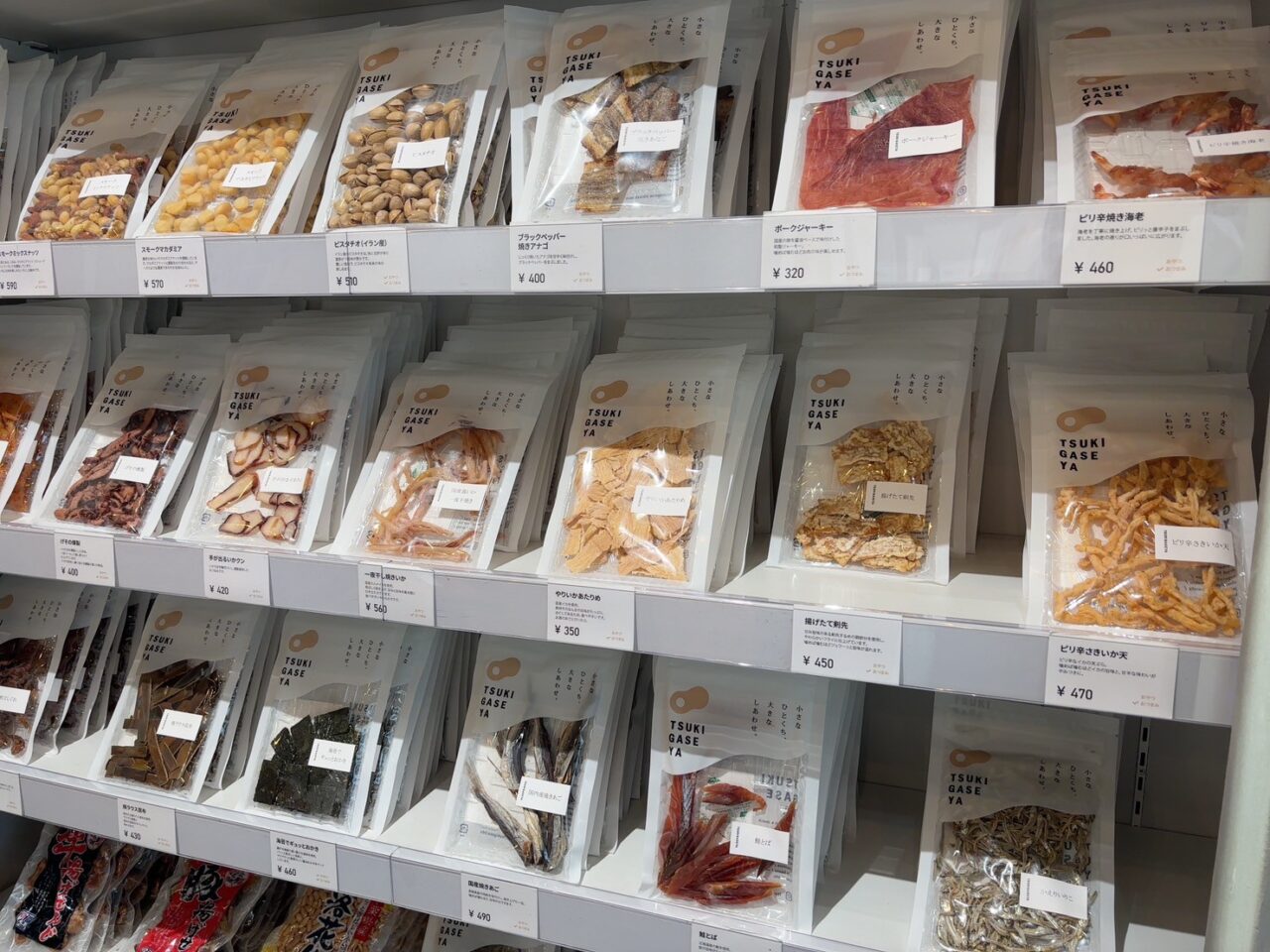 店内の棚に並ぶ「月ヶ瀬」のおつまみやおやつ、色とりどりの商品が見える