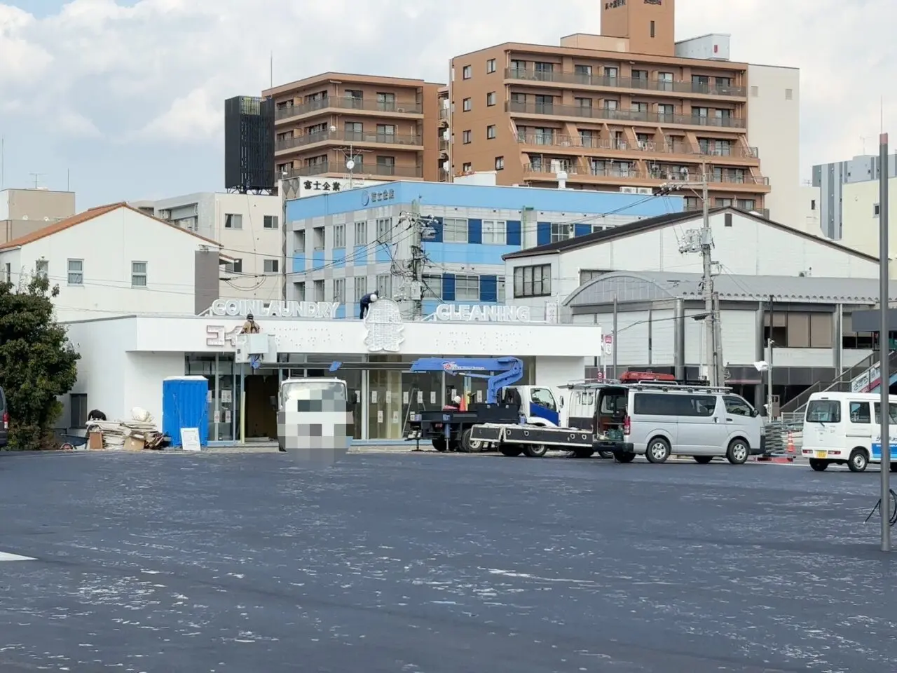 同じ敷地内で建設中の建物に「コインランドリー」「クリーニング」と表示された看板が取り付けられている様子。